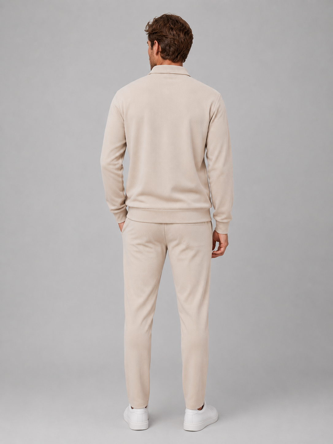 Man wearing beige textured zip jacket and matching trousers two-piece set with white sneakers, shown from behind