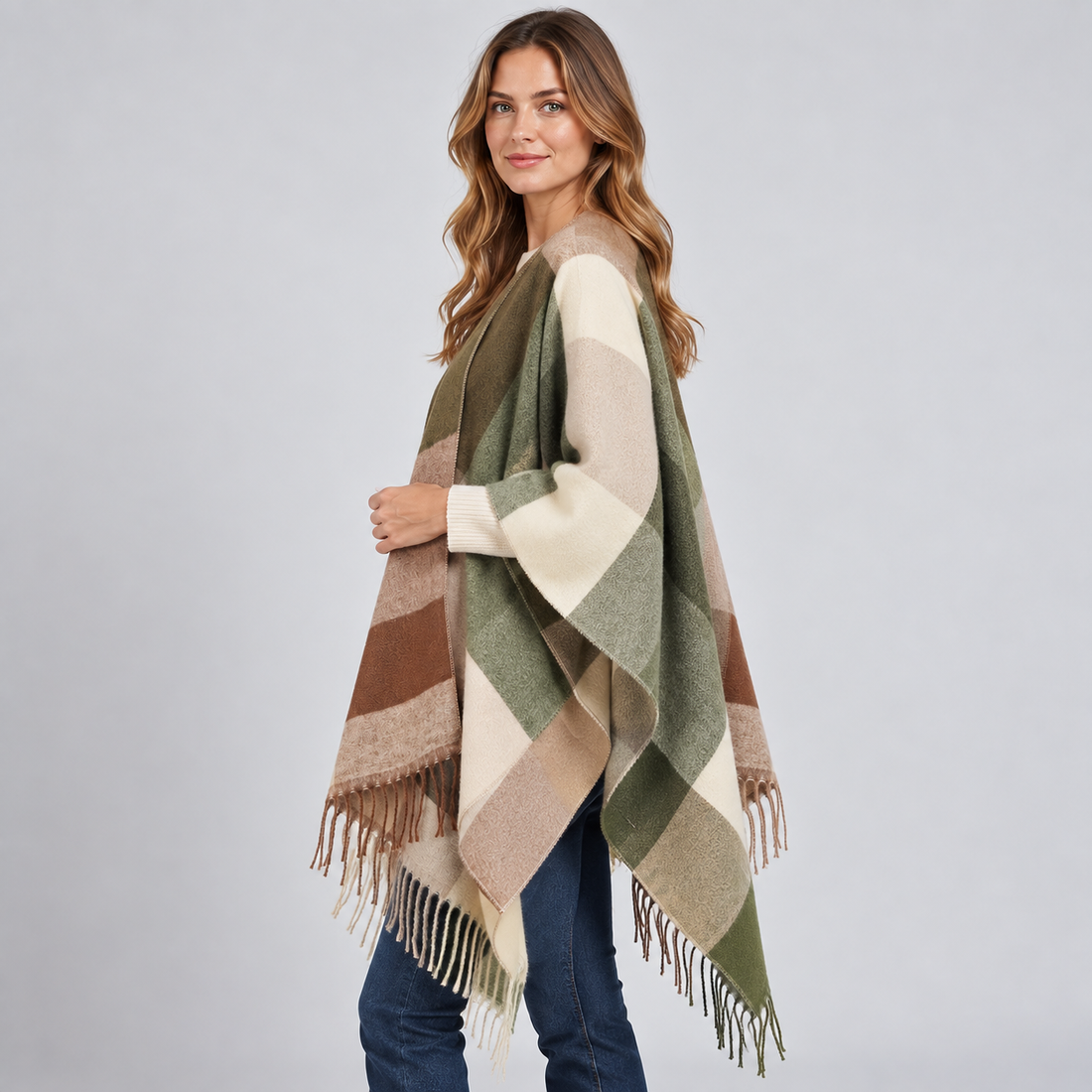 Woman wearing Hadria colour block poncho blanket cape in green, brown and cream with fringe trim and cream long-sleeve top, styled with dark jeans