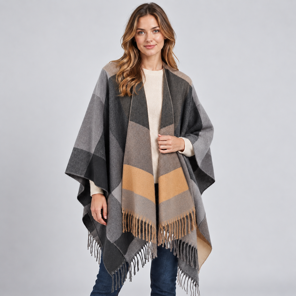 Woman wearing gray, tan, and black color block poncho with fringe trim over cream ribbed sweater and jeans