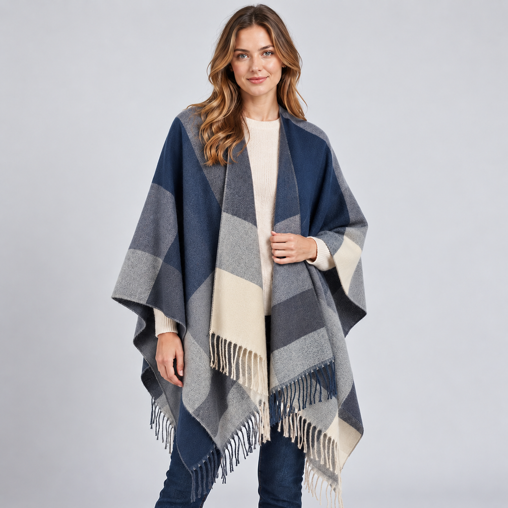 Woman wearing navy, gray and cream color block poncho with fringe trim, styled over white ribbed sweater and dark jeans