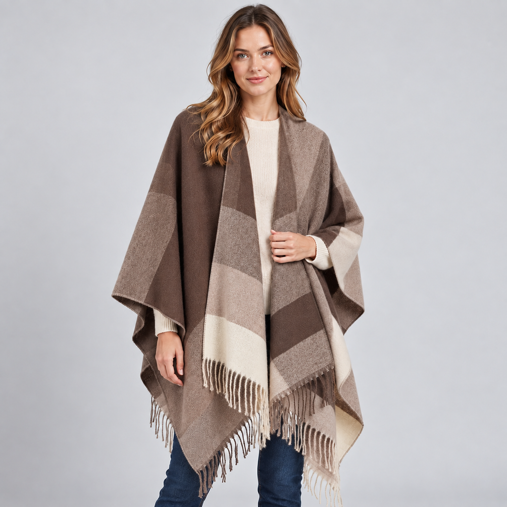 Woman wearing taupe and cream color block poncho with fringe trim over white ribbed shirt and dark jeans