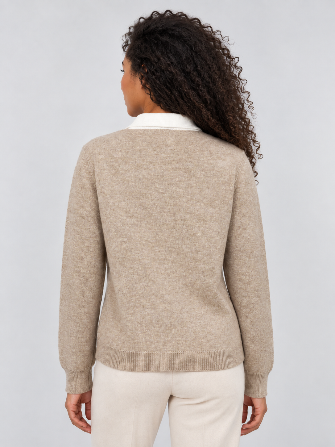 Woman wearing beige knit sweater with white collared neck, viewed from back, showing long sleeves and ribbed hem