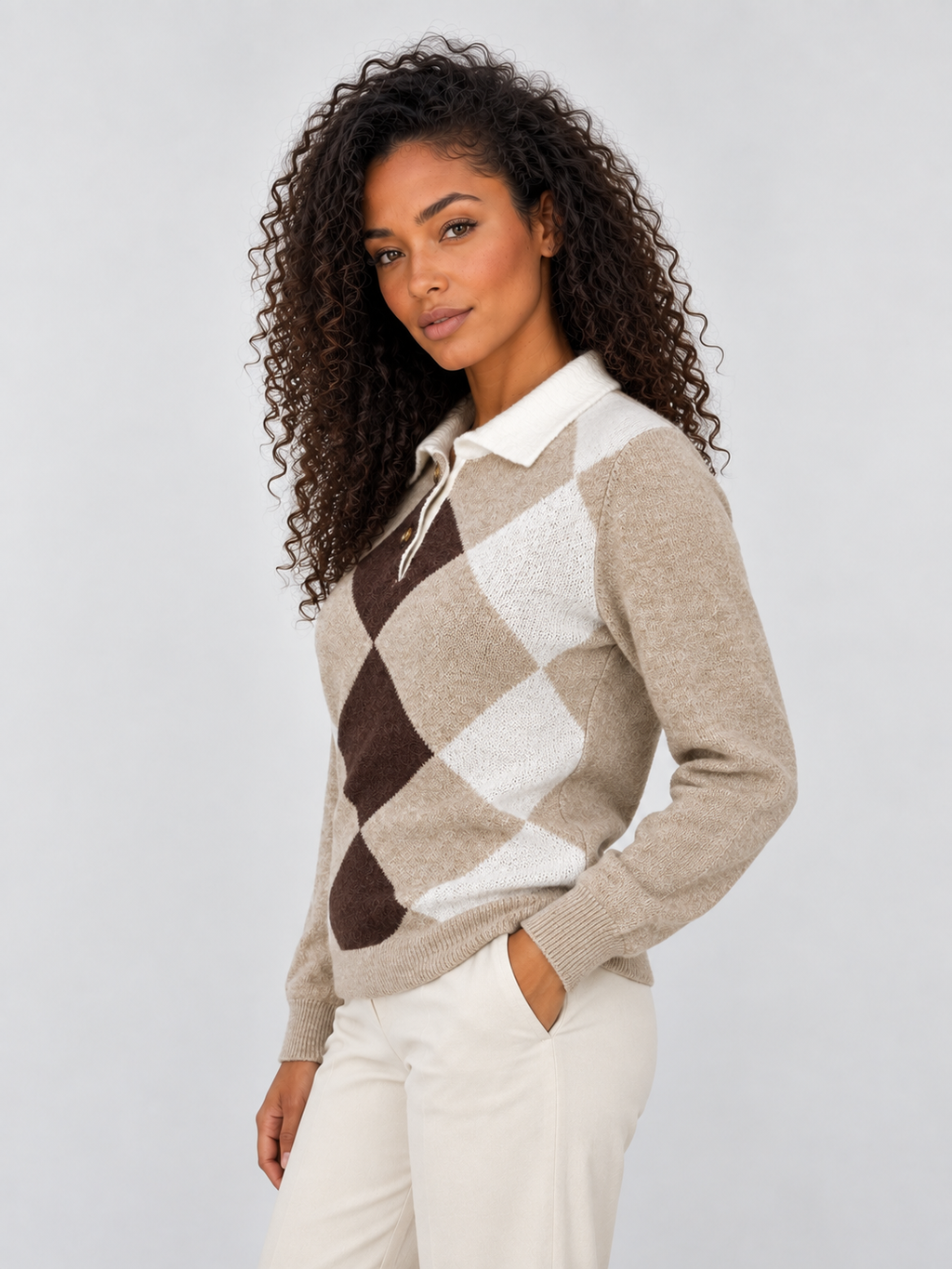 Woman wearing beige, brown and cream argyle collared knit sweater with white pants against neutral background