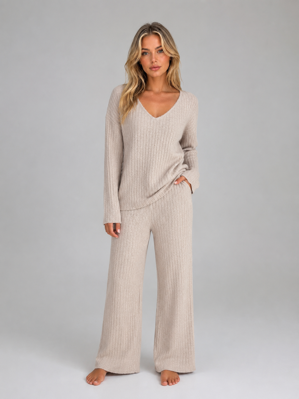 Woman wearing beige ribbed knit V-neck jumper and matching wide leg trousers lounge set, standing against grey background