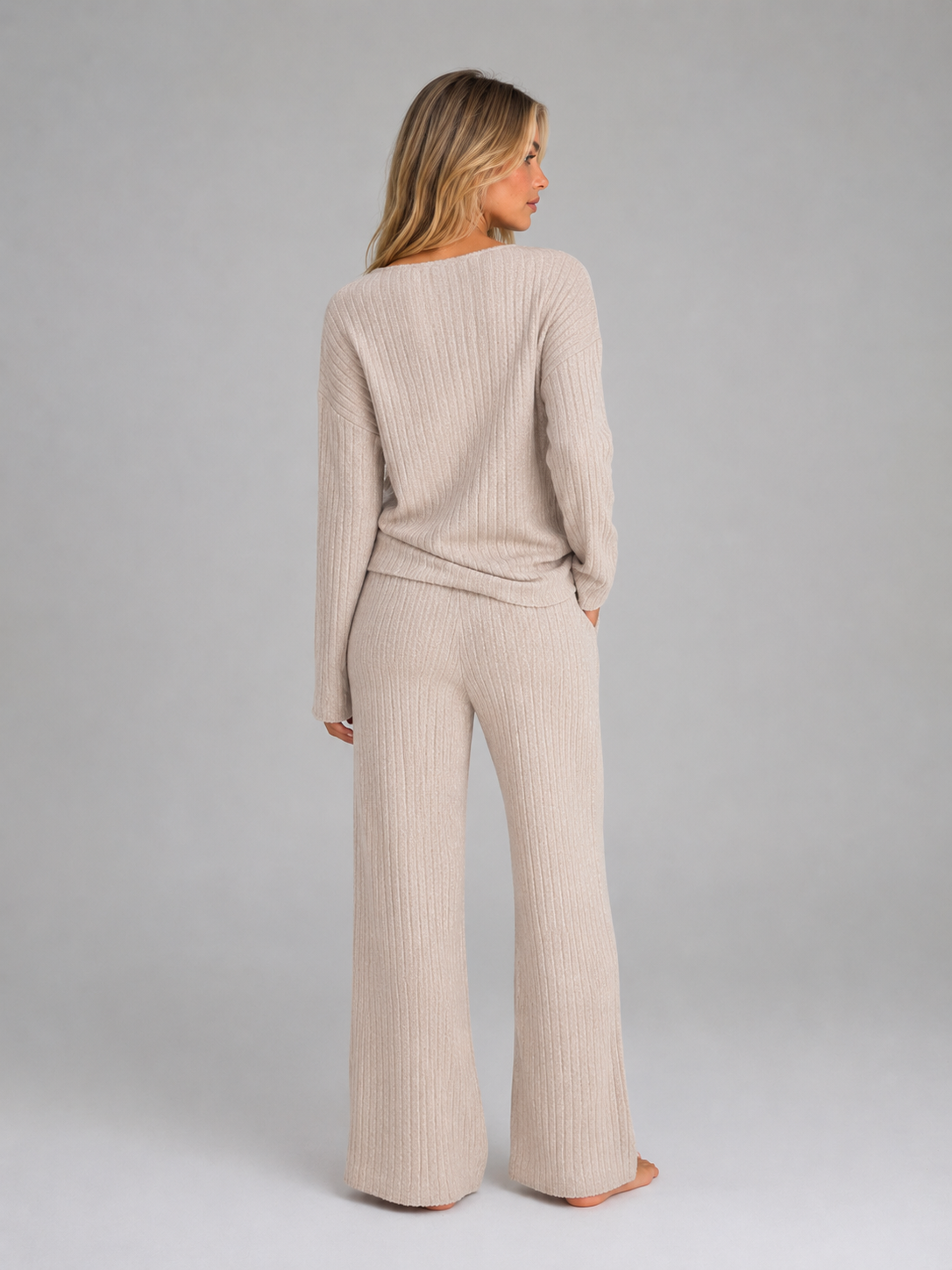 Woman wearing beige ribbed knit V-neck jumper and matching wide leg trousers lounge set, shown from back