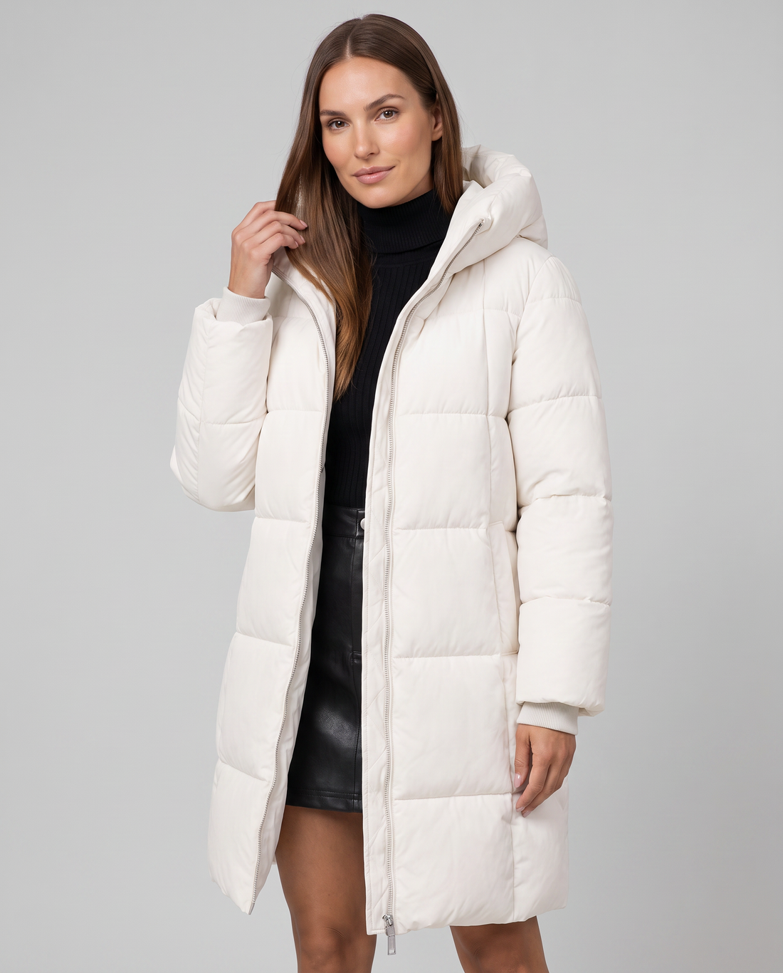Woman wearing cream white hooded quilted puffer coat over black turtleneck and leather skirt