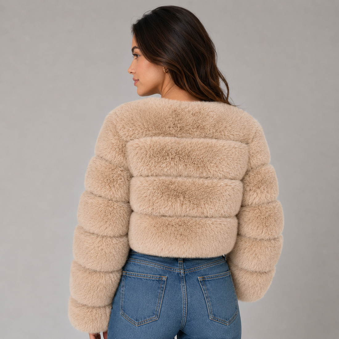 Woman wearing beige cropped fluffy faux fur jacket with puffed sleeves over blue jeans, shown from behind