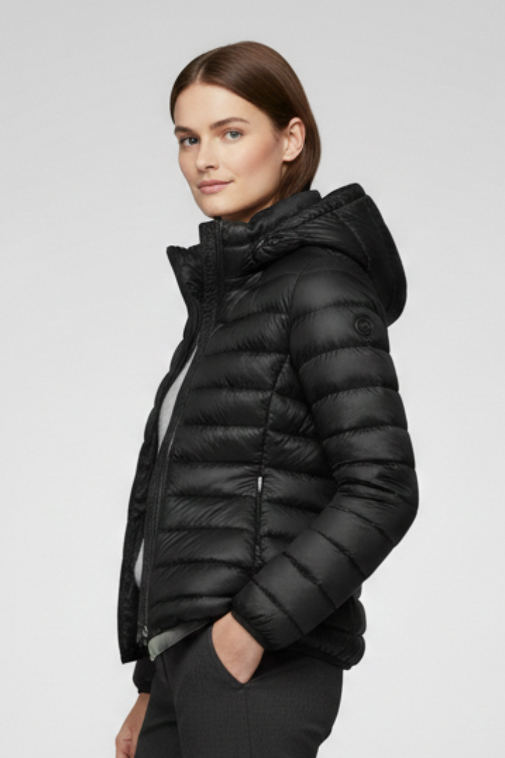 Woman wearing black quilted hooded puffer jacket with zip fastening and hand pockets, displayed against neutral background