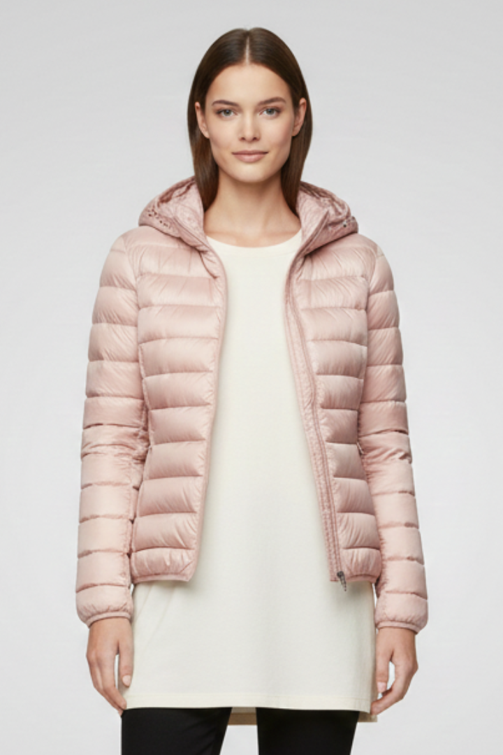 Woman wearing blush pink quilted hooded jacket with zip fastening over cream sweater and black pants against light gray background