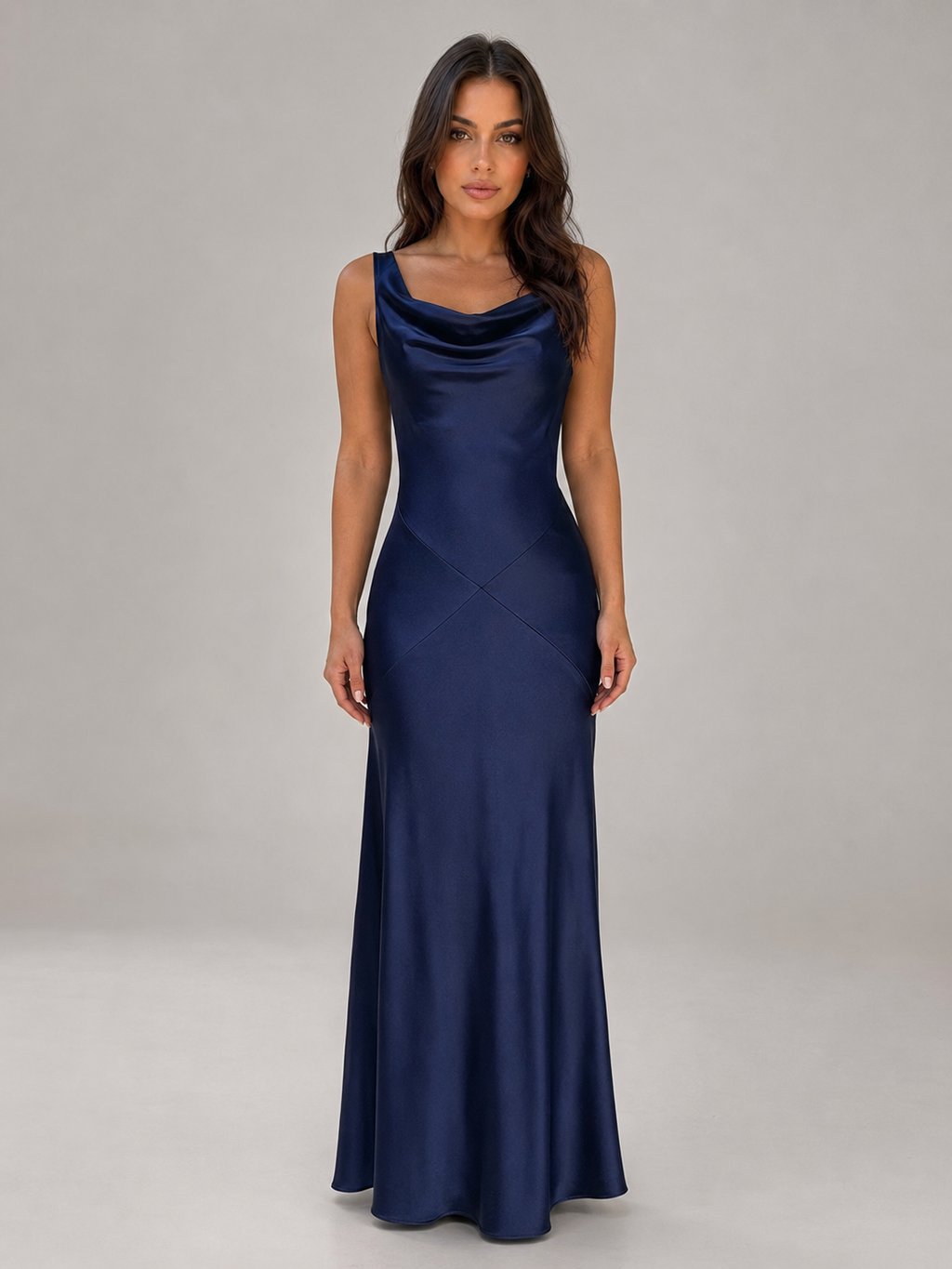 Woman wearing navy sleeveless satin maxi dress with cowl neckline and open back, standing against neutral background