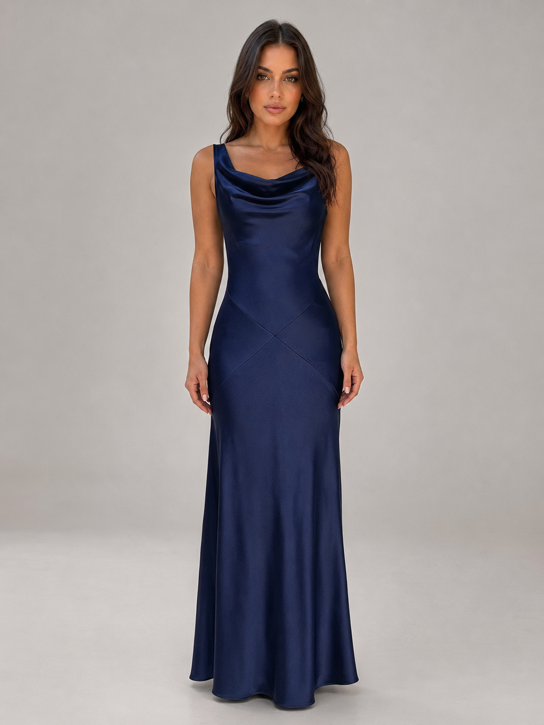Woman wearing navy sleeveless satin maxi dress with cowl neckline and open back, standing against neutral background