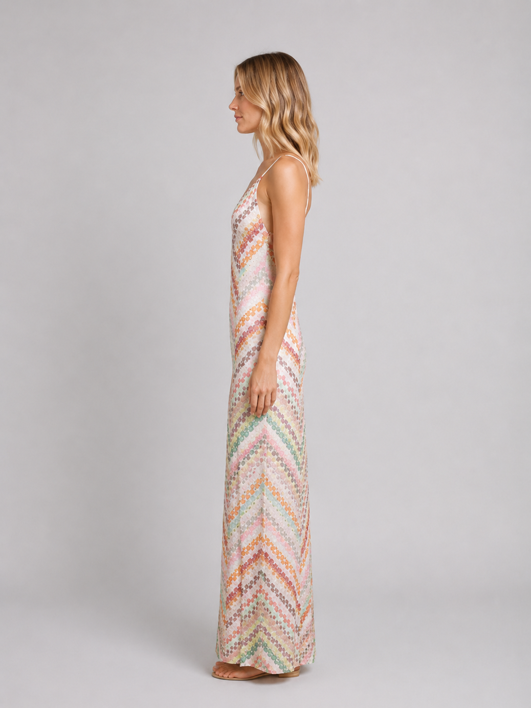 Woman wearing multicolored striped crochet knit maxi dress with chevron pattern in pastel pink, orange, and green tones