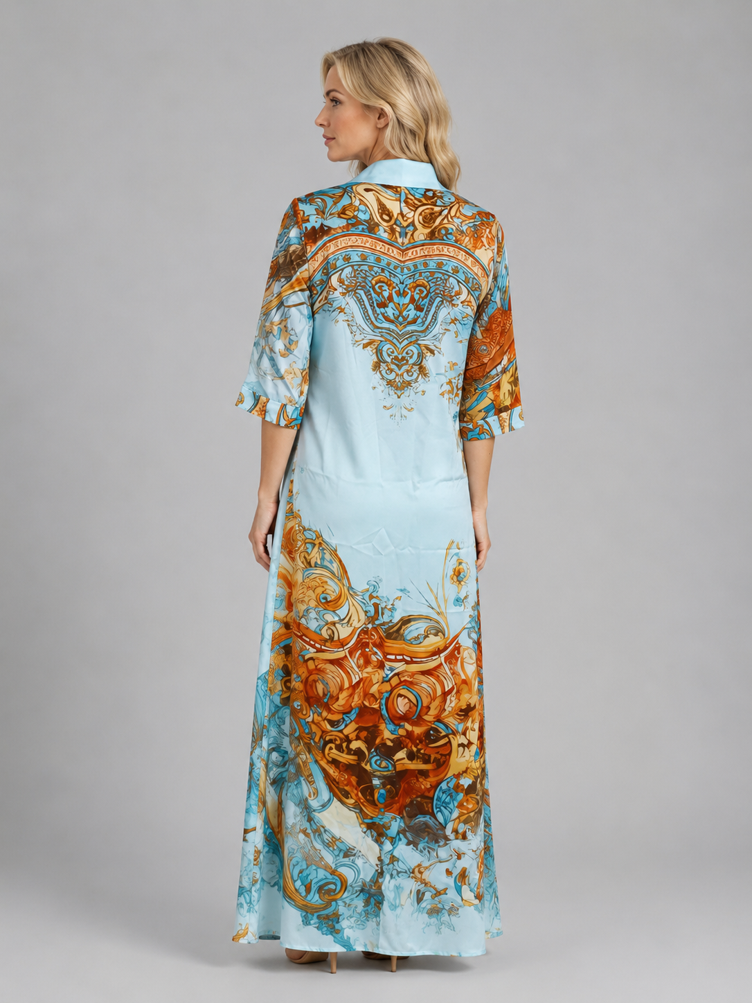Woman wearing light blue button-front maxi dress with ornate gold and teal baroque print, three-quarter sleeves, shown from back