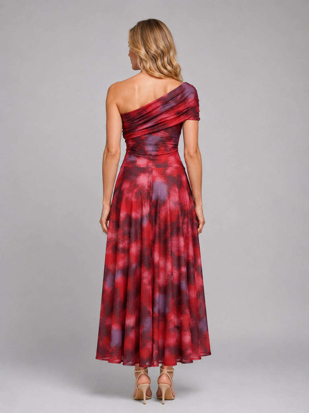 Woman wearing red tie-dye one-shoulder maxi dress with flowing skirt and tan heeled sandals, back view