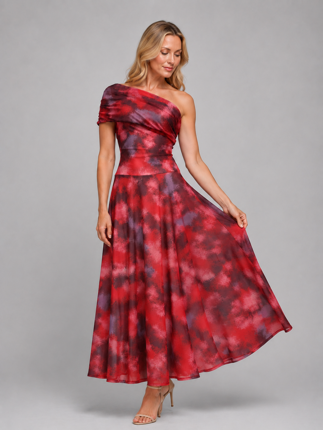 Woman wearing red and purple tie-dye one-shoulder maxi dress with flowing skirt and short sleeve, paired with tan heels