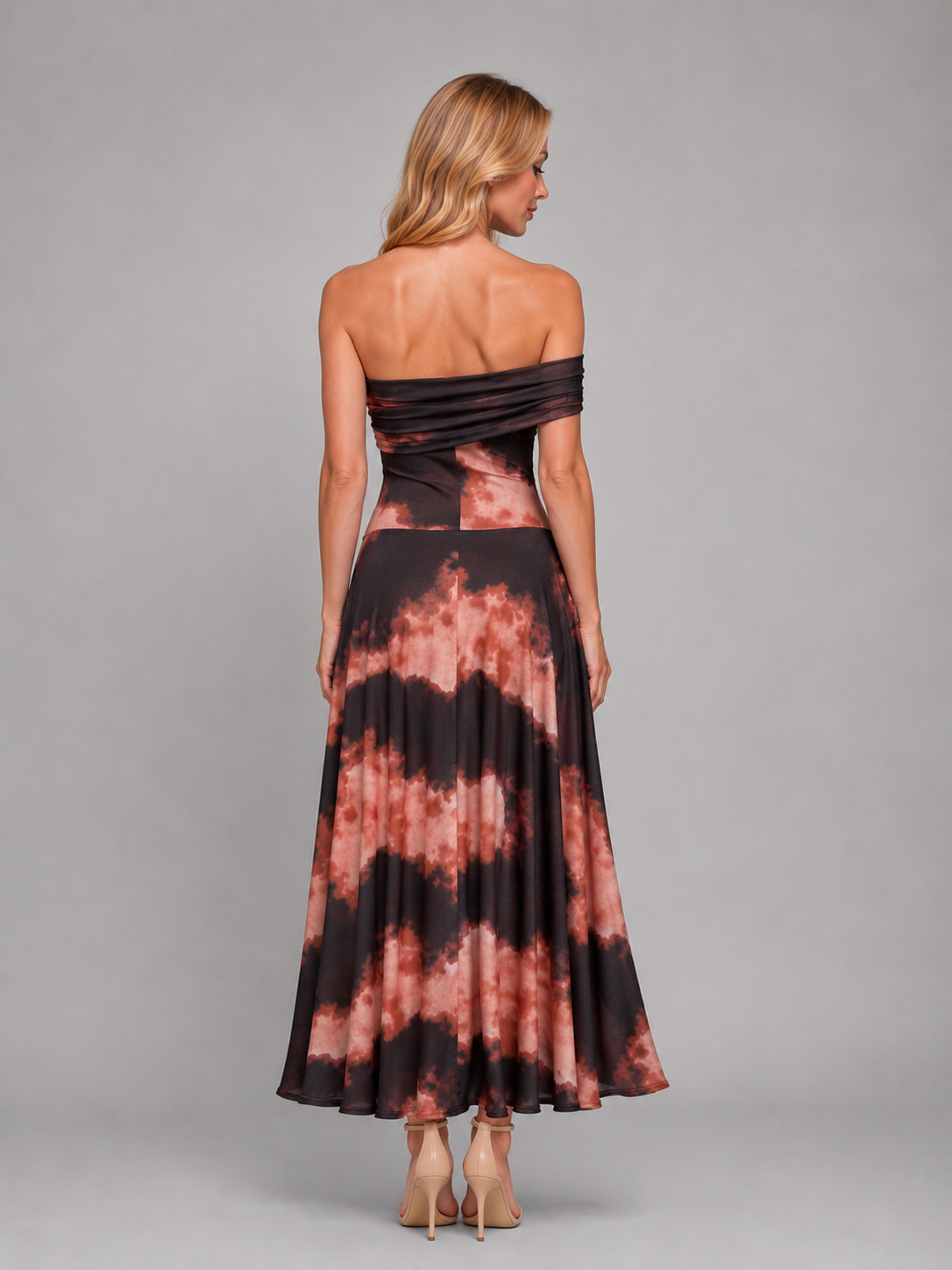 Woman wearing black and coral tie-dye one-shoulder maxi dress with flowing skirt, shown from back view wearing nude heels