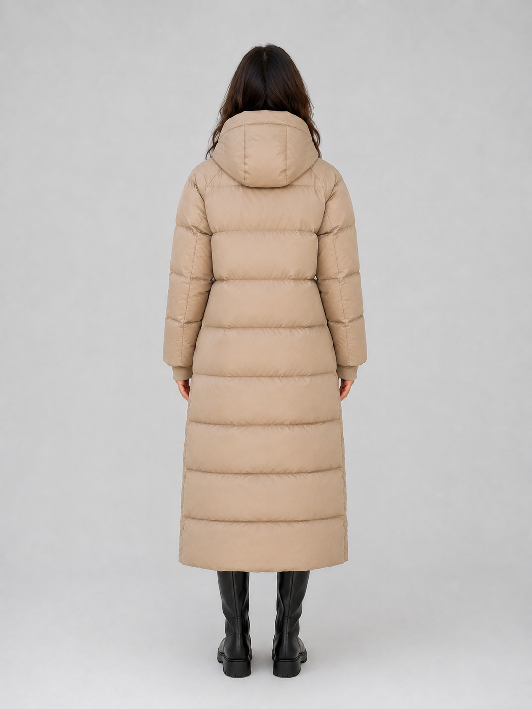 Woman wearing beige hooded padded long puffer winter coat with black boots, shown from back view