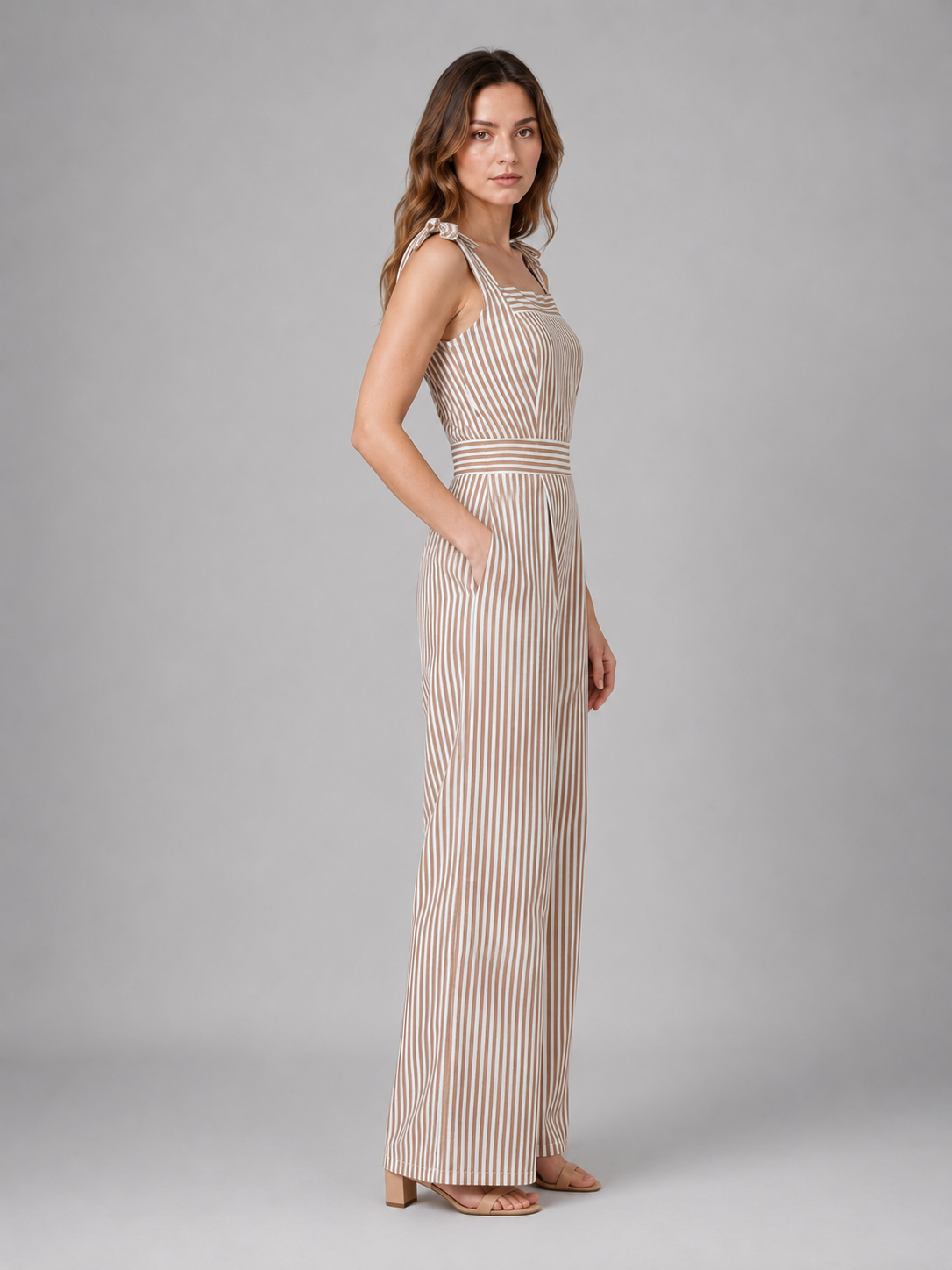 Woman wearing beige and white striped wide leg jumpsuit with tie shoulder straps and cutout waist detail