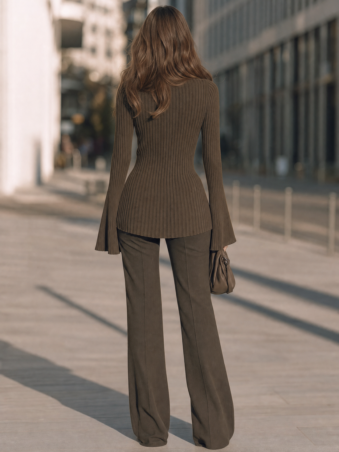 Woman wearing taupe ribbed bell-sleeve mock-neck sweater with high-low hem and olive flare pants, standing on urban street