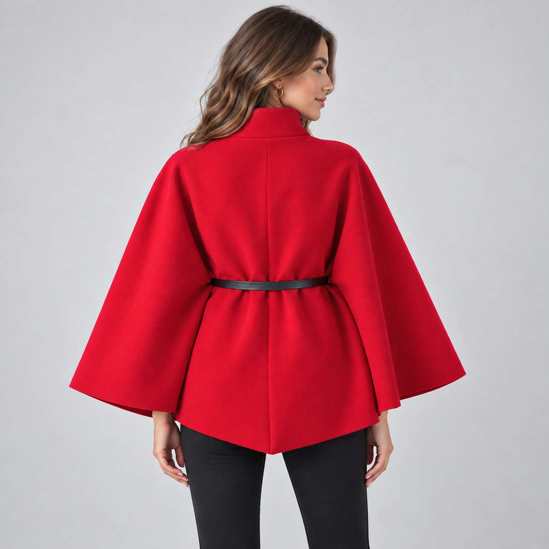 Woman wearing red high neck belted cape coat with black pants, shown from behind against white background