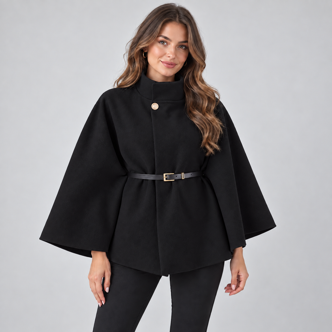 Woman wearing black high neck belted cape coat with gold button and belt, styled over black pants
