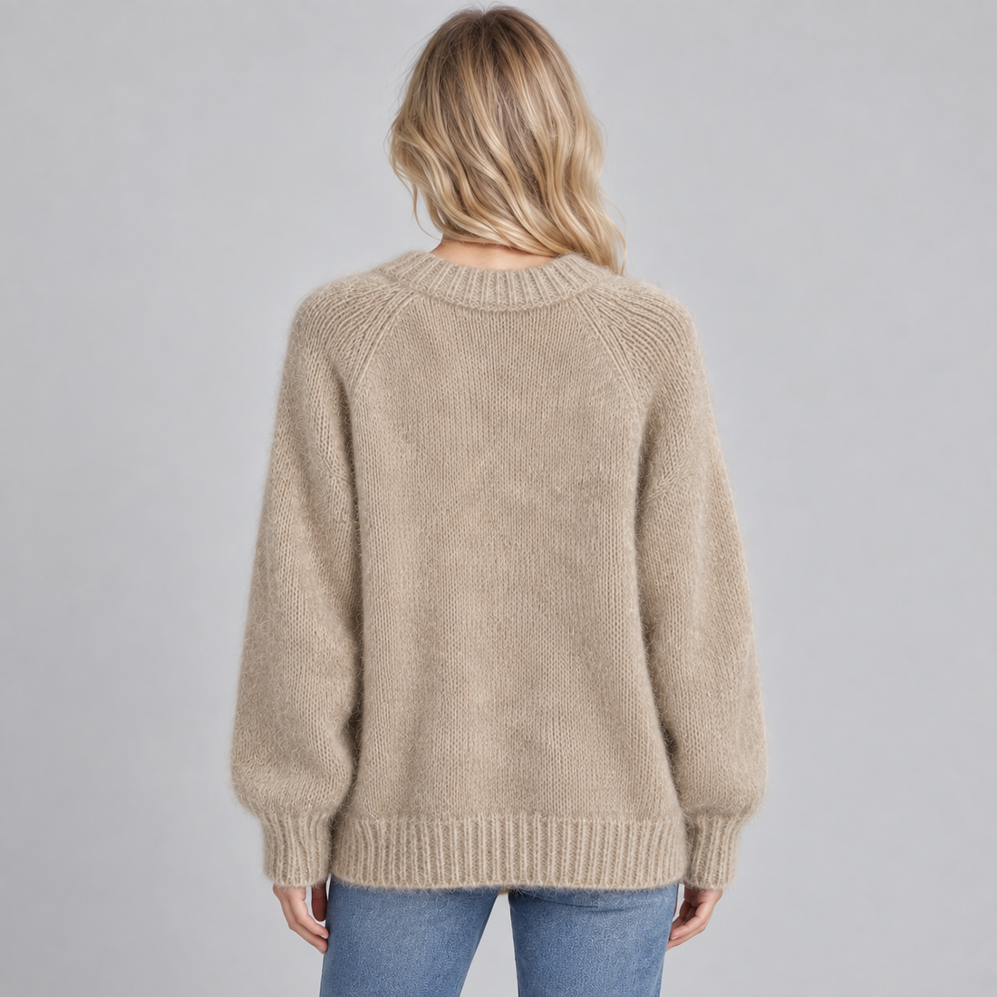 Woman wearing a beige round neck fluffy knit jumper with long raglan sleeves, viewed from behind, paired with blue jeans