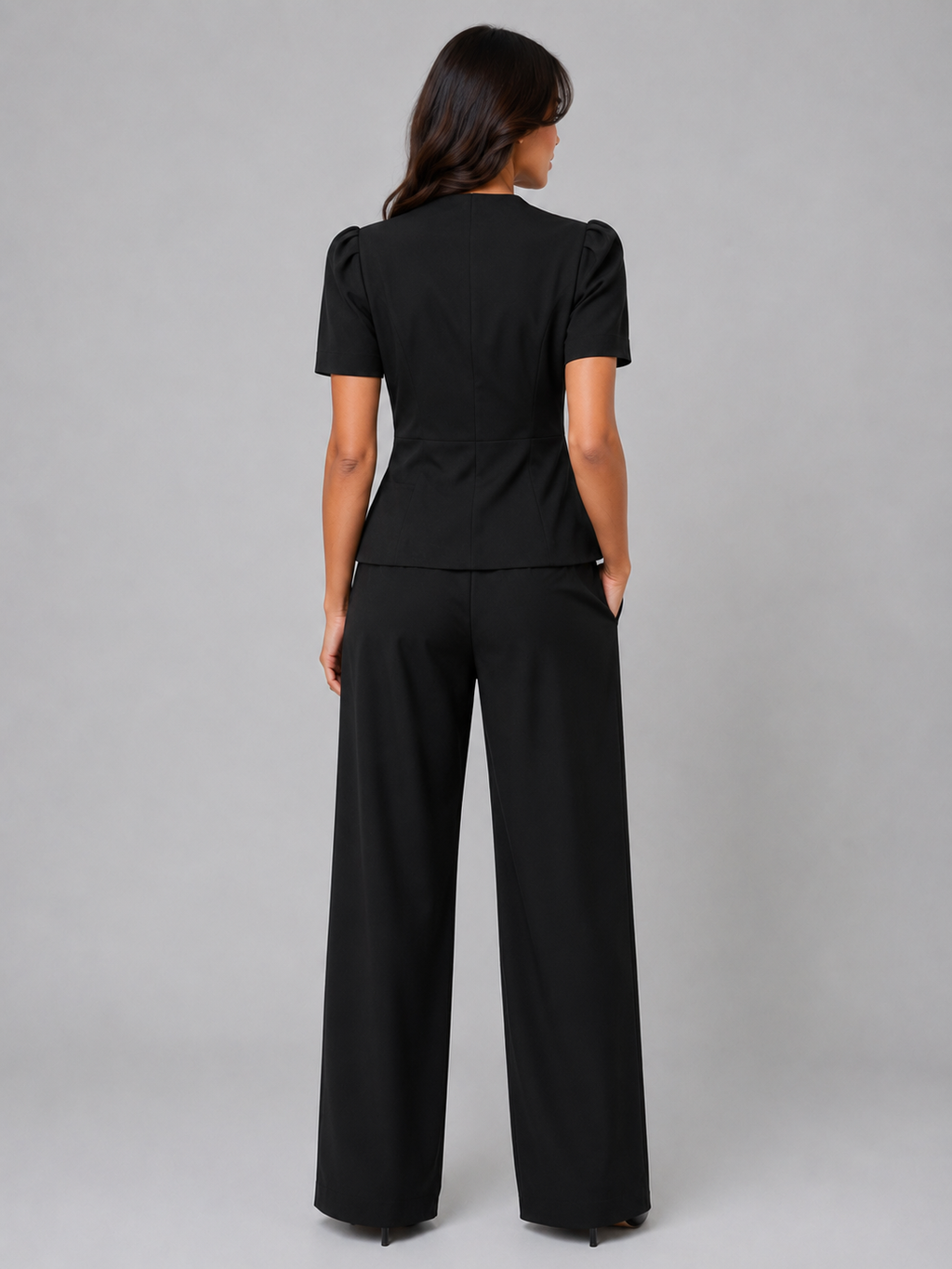 Woman wearing black short sleeve blazer and wide leg trousers suit set, back view, gray background