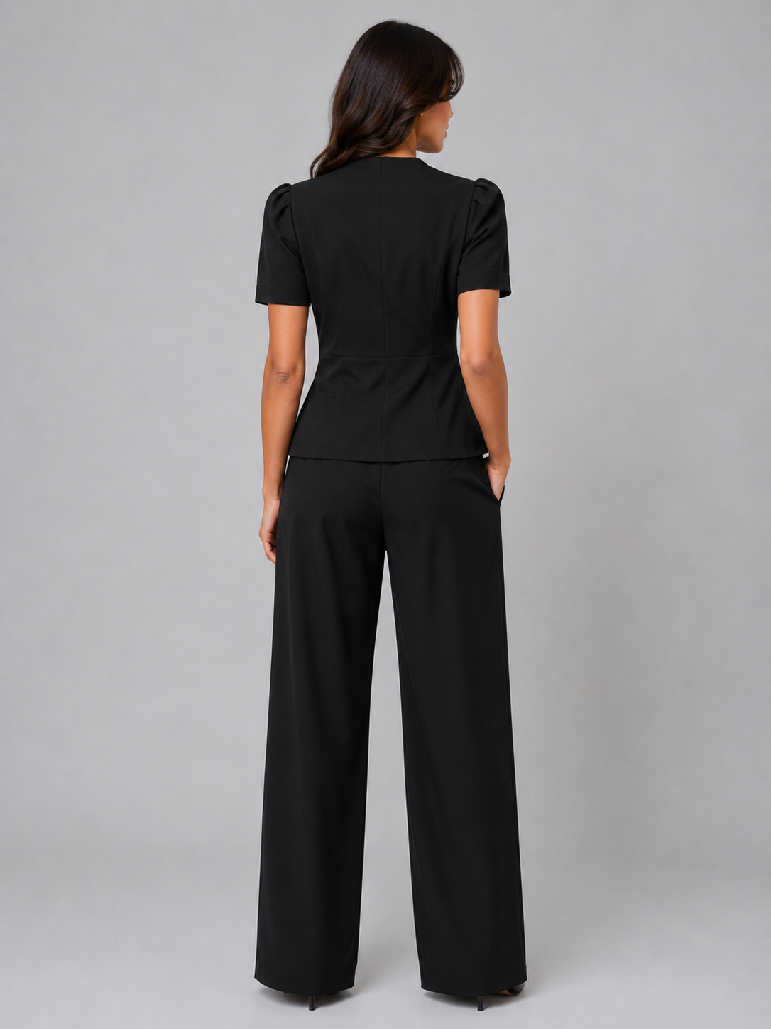 Woman wearing black short sleeve blazer and wide leg trousers suit set, back view, gray background