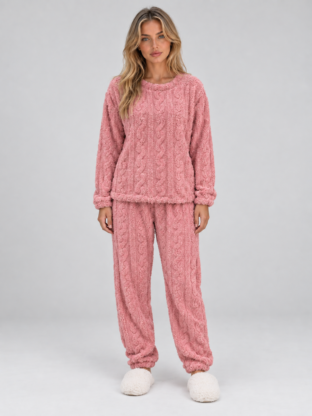 Woman wearing pink cable knit thermal fleece pajama set with long sleeves and matching pants, styled with white fuzzy slippers