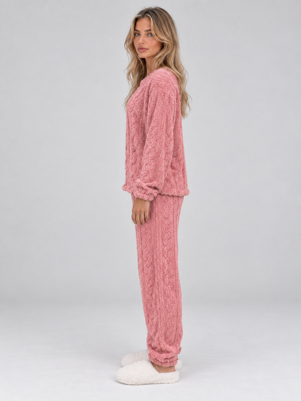 Woman wearing pink cable knit thermal fleece pyjama set with long sleeves and matching trousers, white slippers