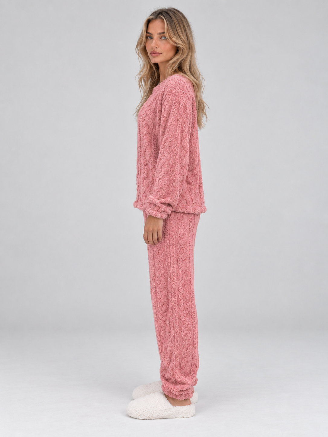 Woman wearing pink cable knit thermal fleece pyjama set with long sleeves and matching trousers, white slippers