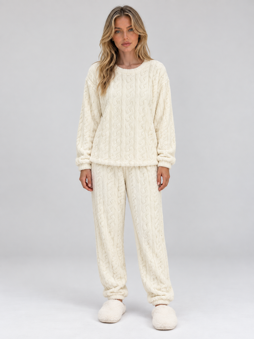 Woman wearing cream cable knit thermal fleece pajama set with long sleeves and matching pants, styled with white slippers
