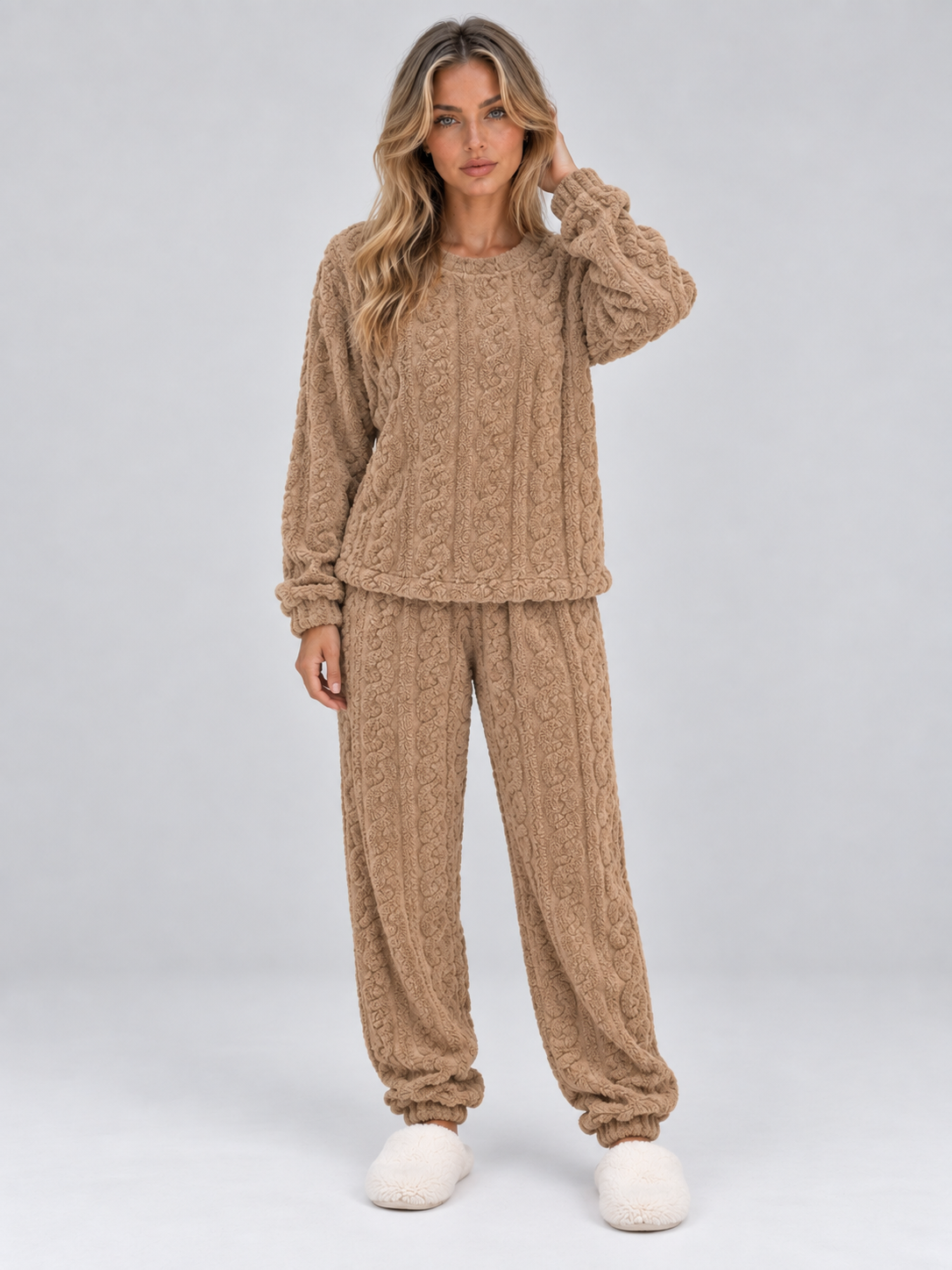 Woman wearing beige cable knit thermal fleece pyjama set with long sleeves and matching trousers, paired with white fuzzy slippers
