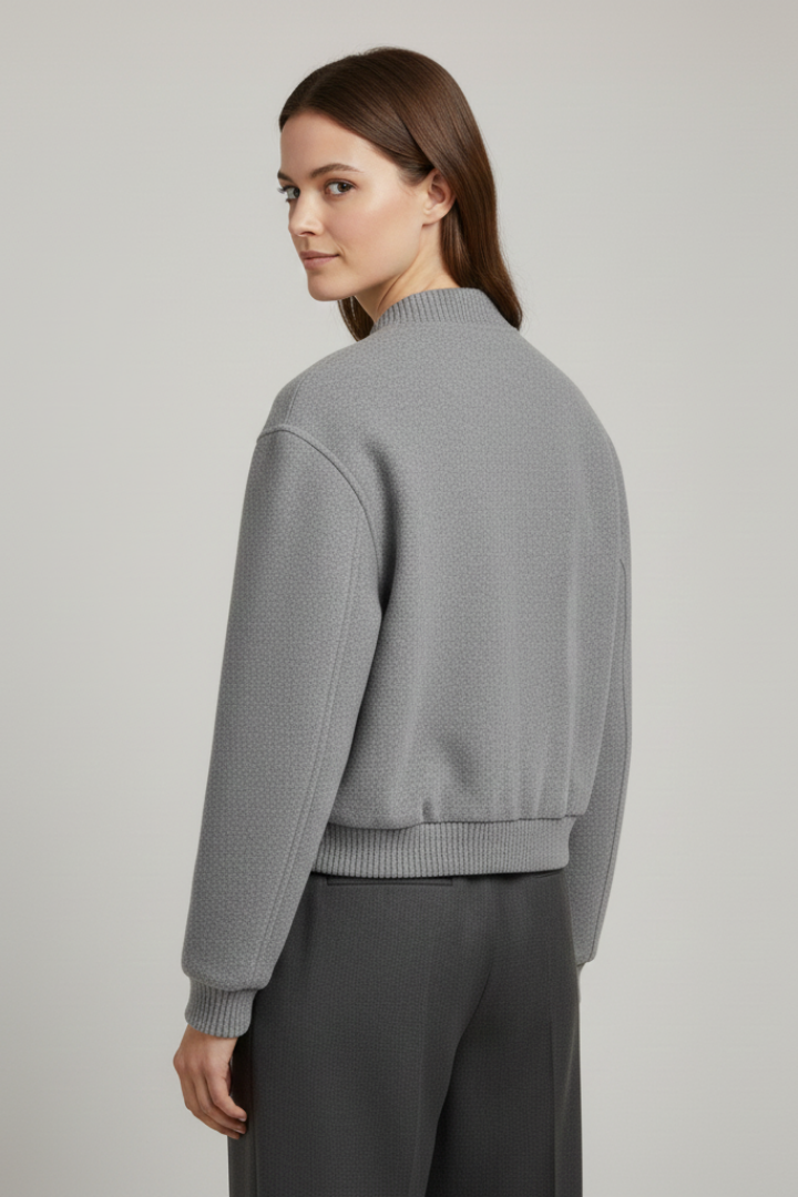Woman wearing gray cropped snap fastening jacket with ribbed cuffs and dark pants, rear view