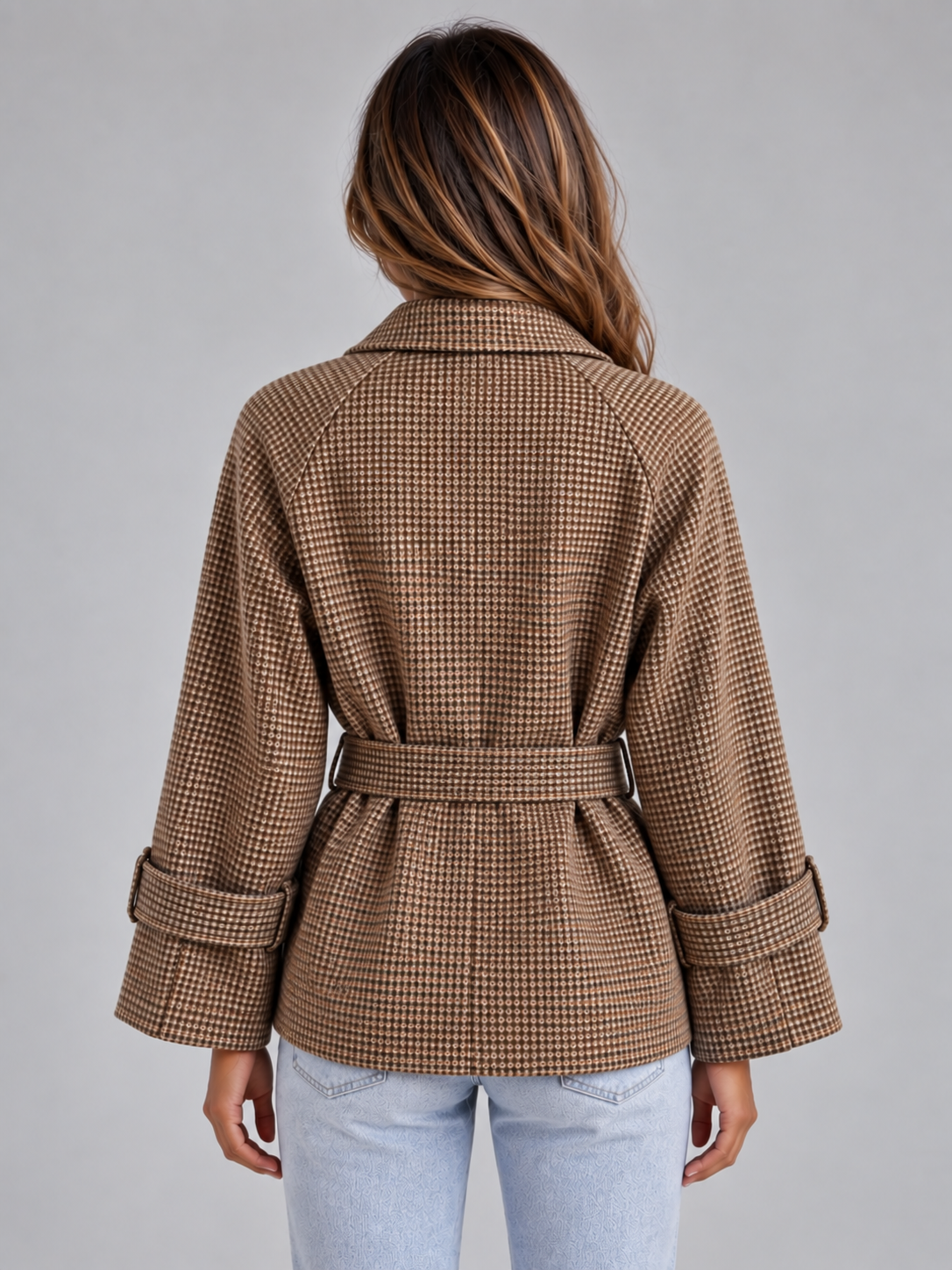 Woman wearing camel and cream check pattern belted trench coat with rolled sleeves and blue jeans, back view