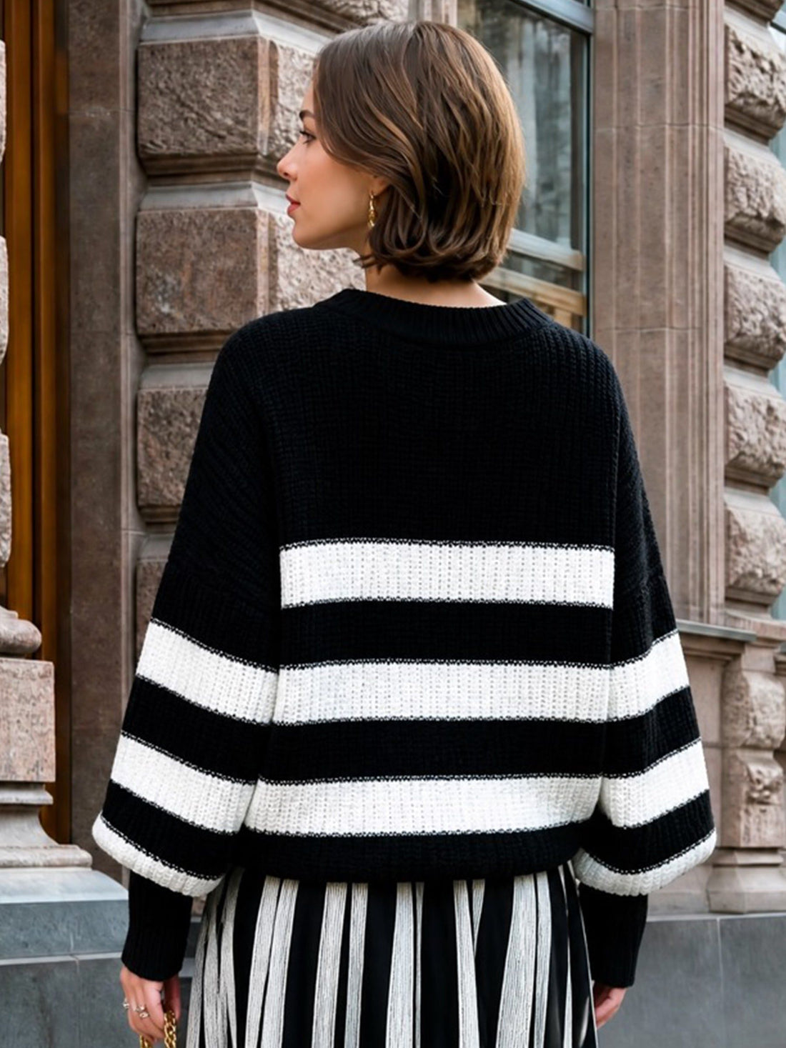 Woman wearing black and white striped relaxed knit sweater with horizontal stripes, standing against stone building