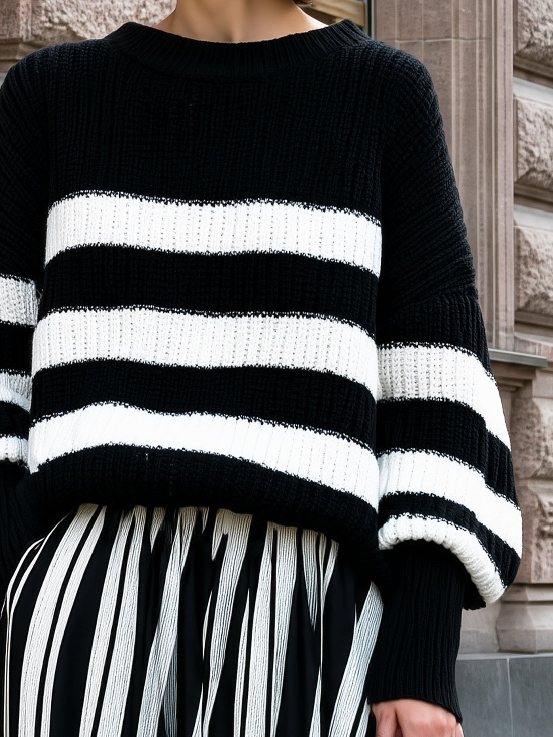 Woman wearing black and white striped ribbed knit sweater with relaxed fit, displayed against brick wall background