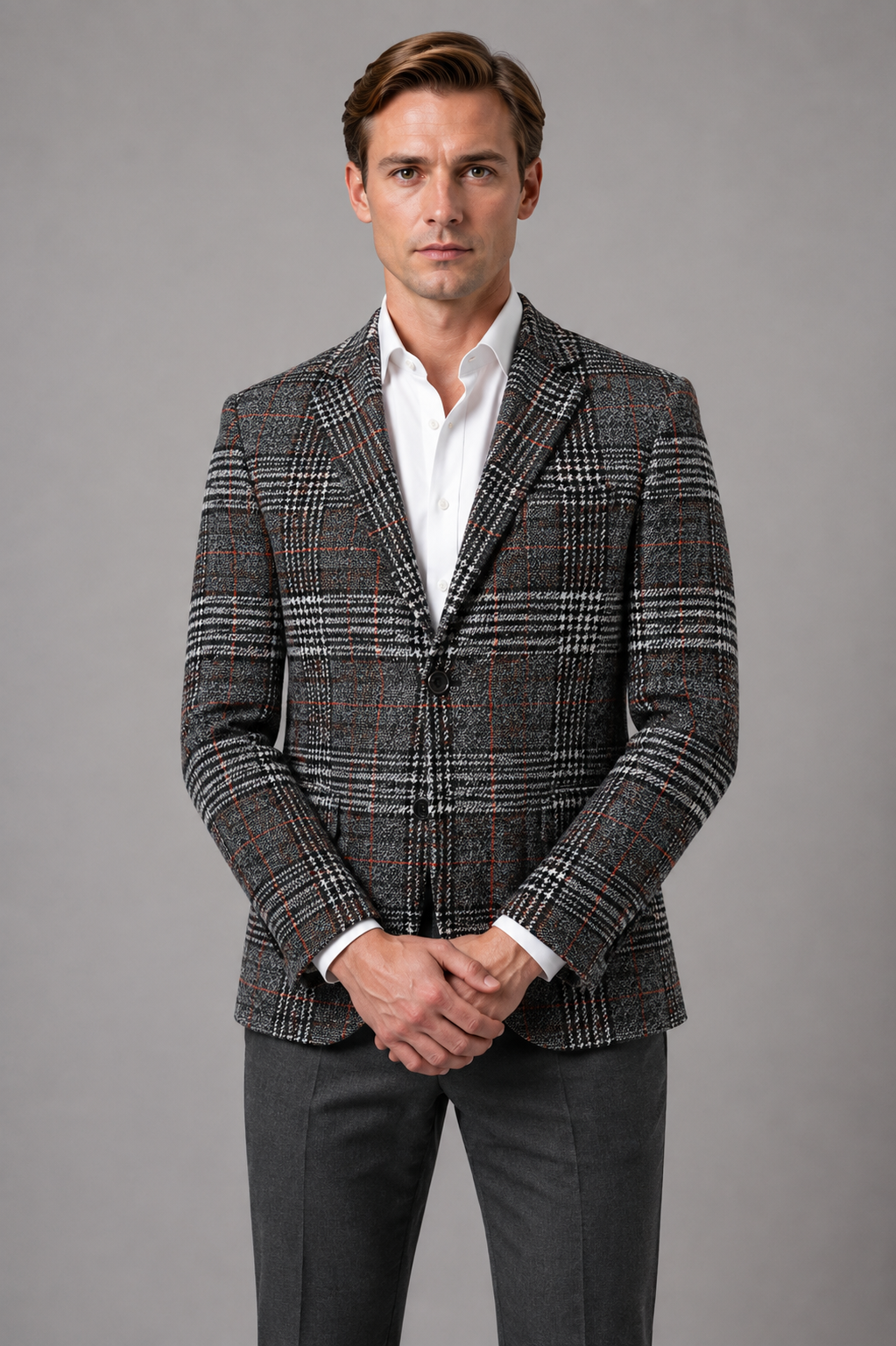 Man wearing charcoal plaid tweed blazer with white dress shirt and dark trousers, standing against gray background