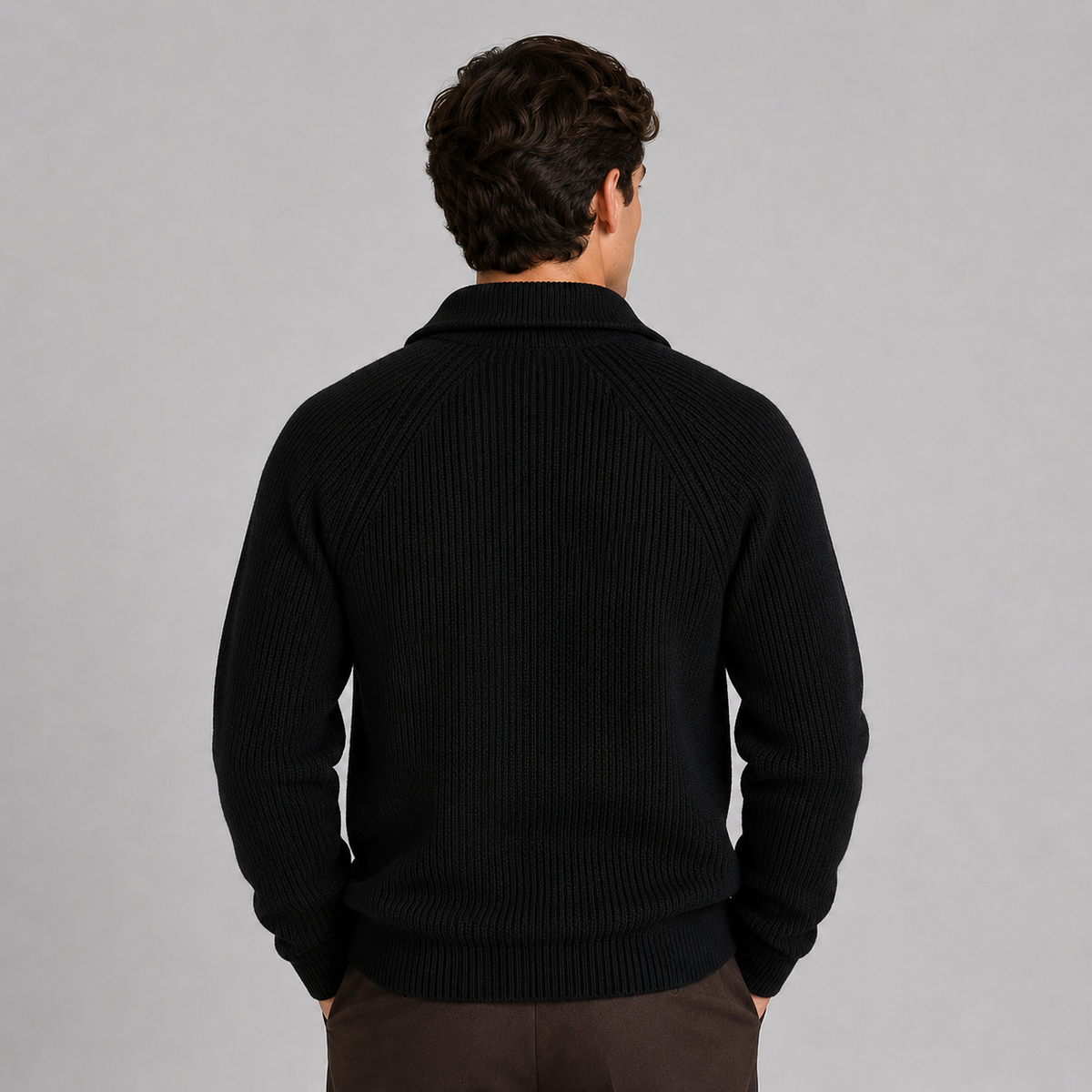 Man wearing black quarter-zip ribbed knit sweater with brown trousers, shown from back view against gray background