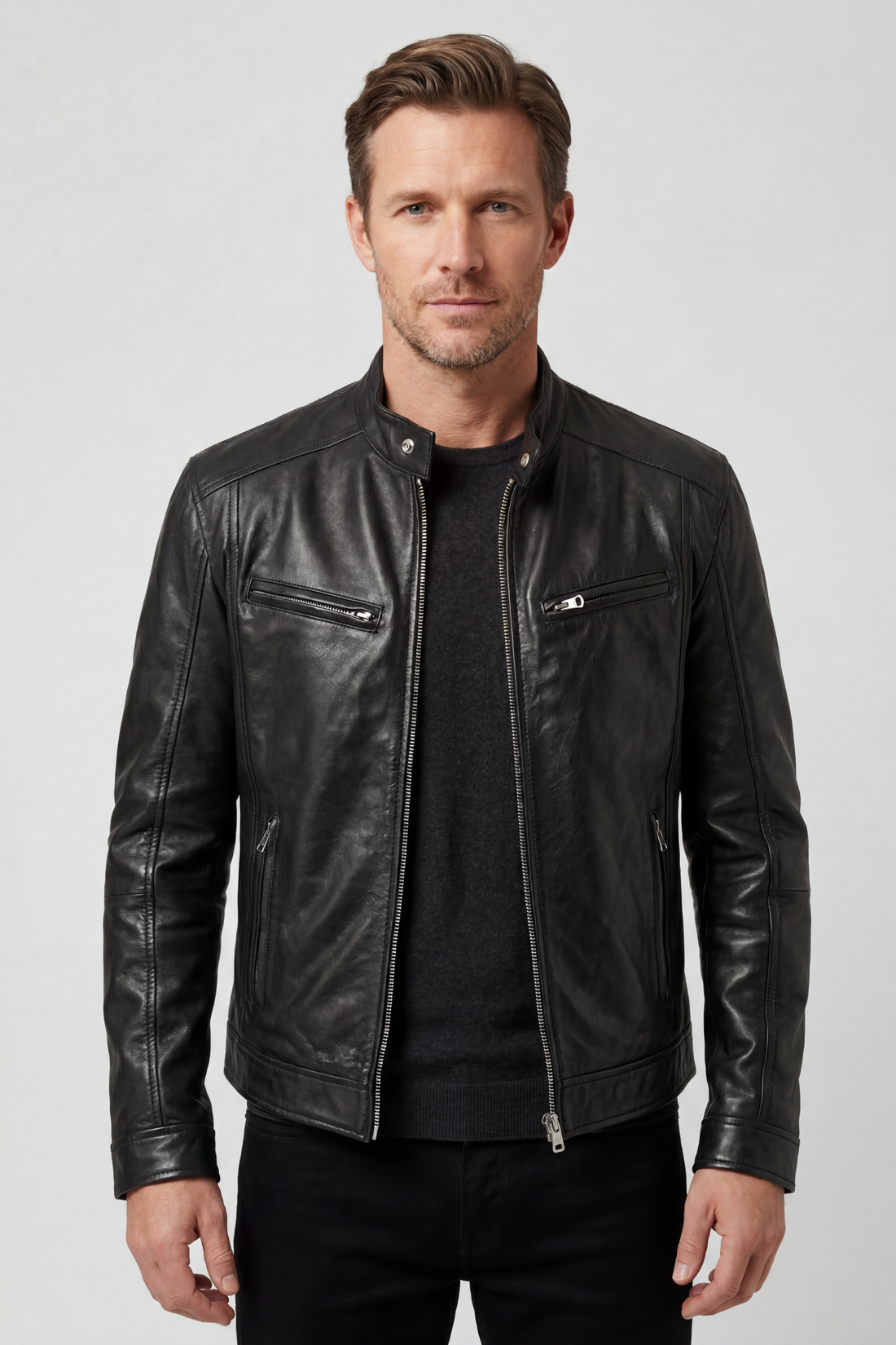 Man wearing black leather jacket with zip pockets and dark sweater, standing against neutral background