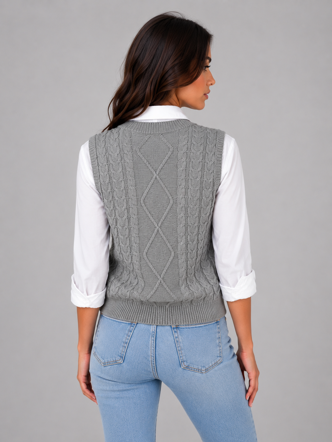 Woman wearing gray cable knit sleeveless sweater vest over white collared shirt with light blue jeans