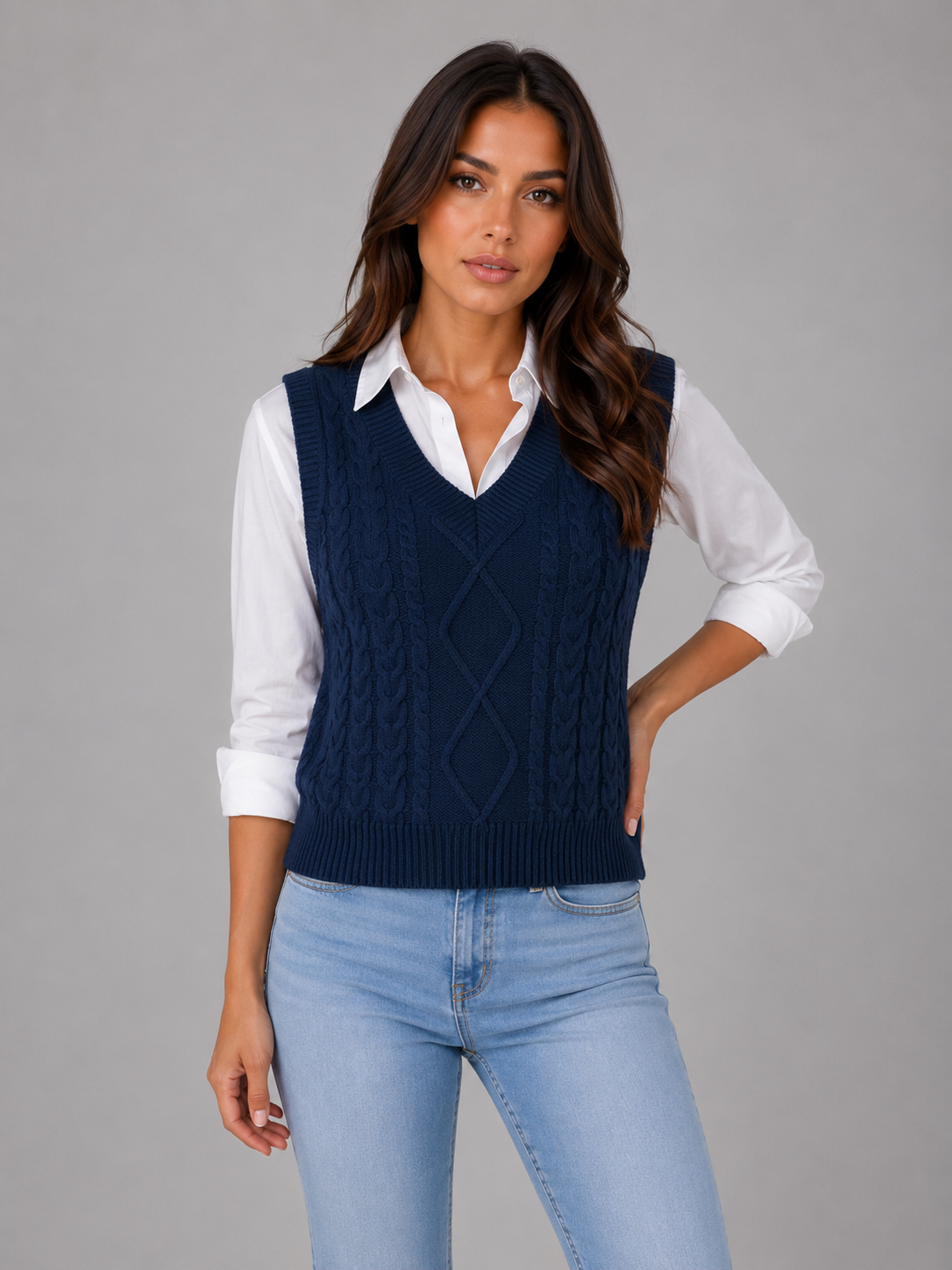 Woman wearing navy blue cable knit V-neck sleeveless sweater vest over white collared shirt with light blue jeans
