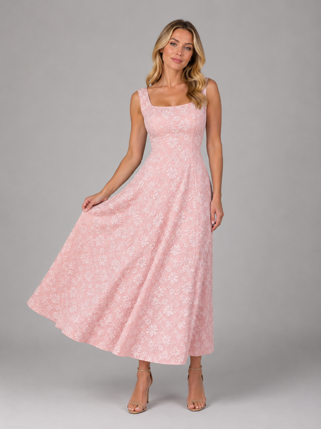 Woman wearing pink floral jacquard sleeveless midi dress with square neckline and full skirt, paired with nude heeled sandals