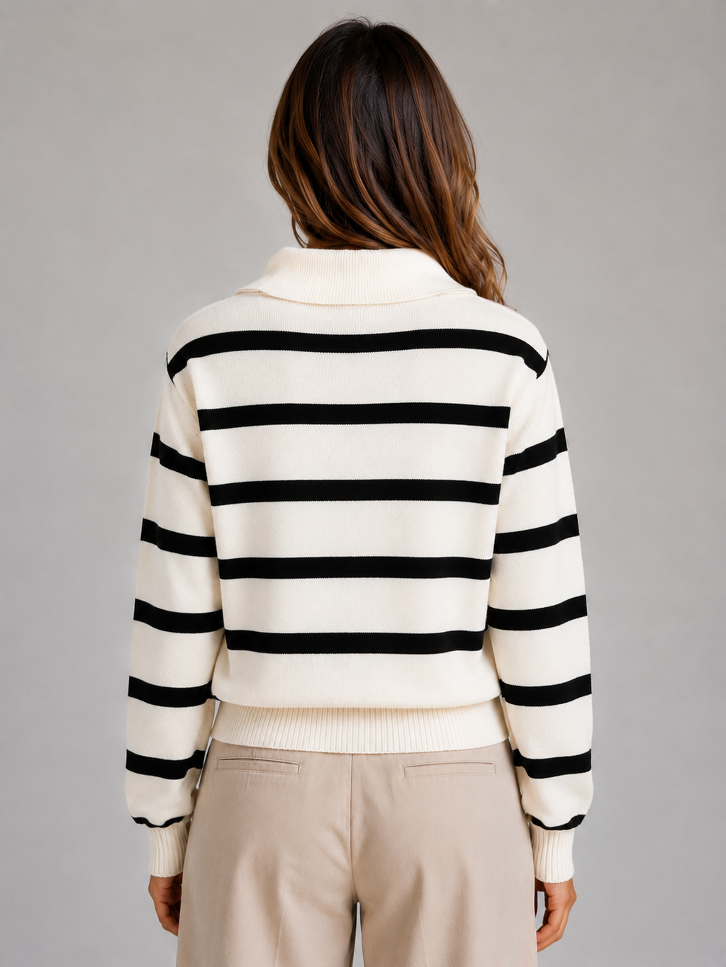 Woman wearing cream and black striped knitted jumper with relaxed collar and half-zip, beige pants, back view