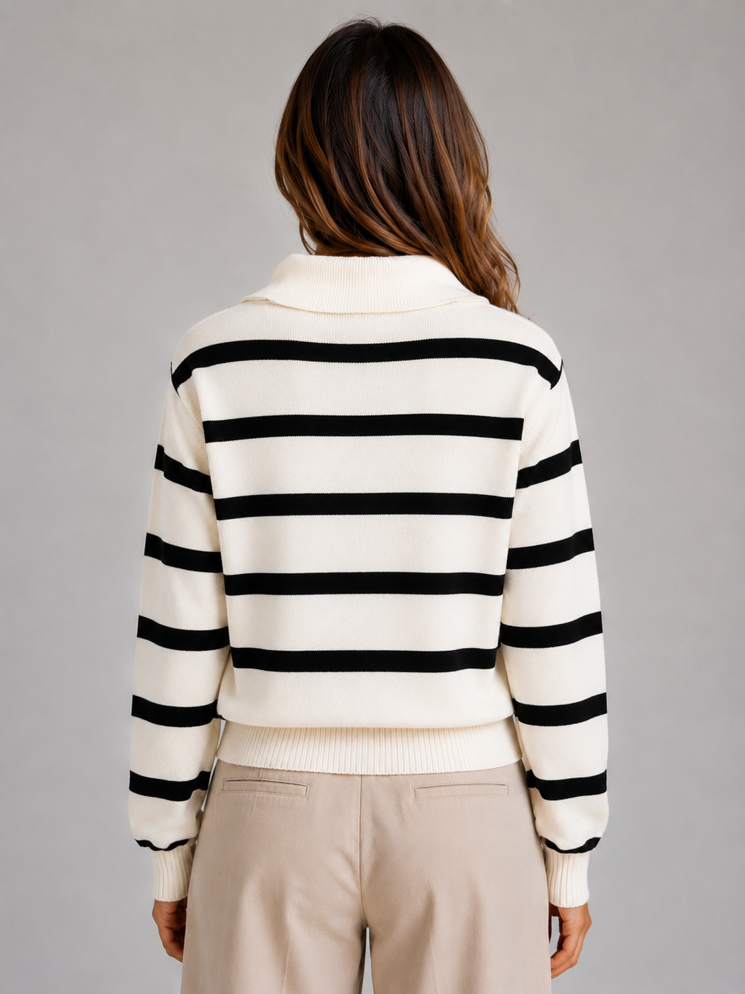 Woman wearing cream and black striped knitted jumper with relaxed collar and half-zip, beige pants, back view