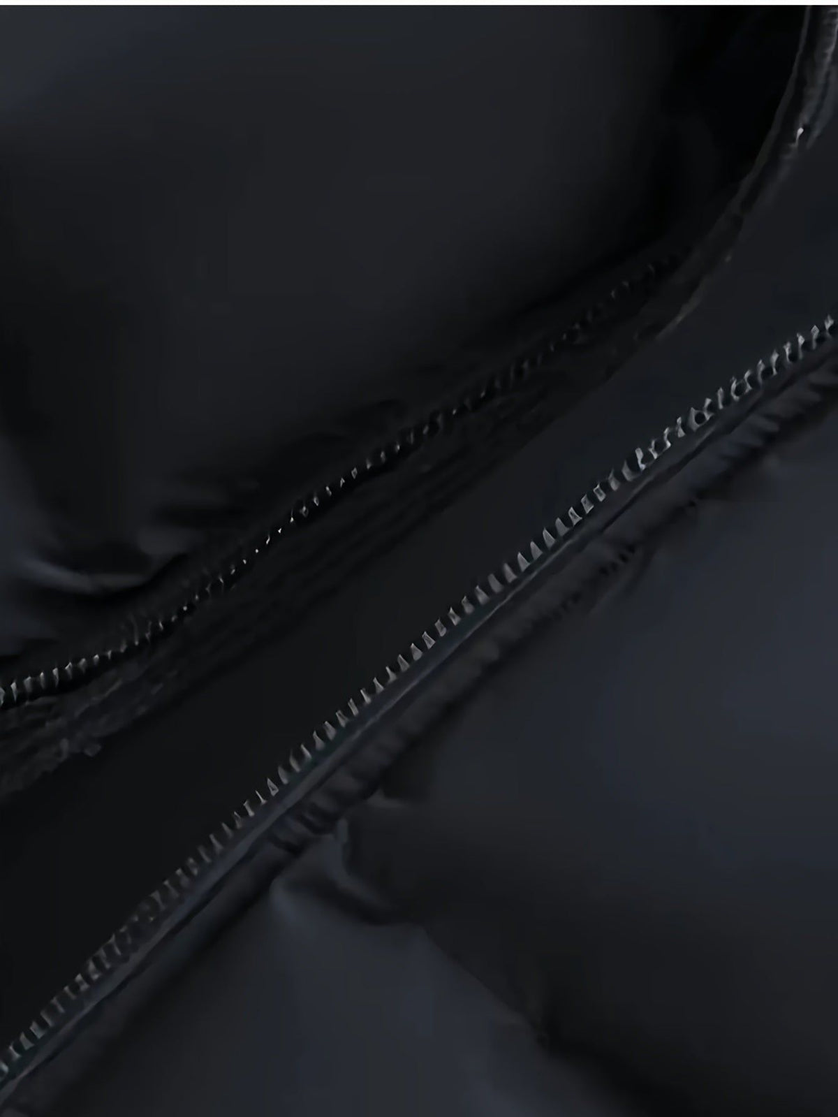 Close-up of metal zipper on black padded puffer jacket with detailed stitching visible