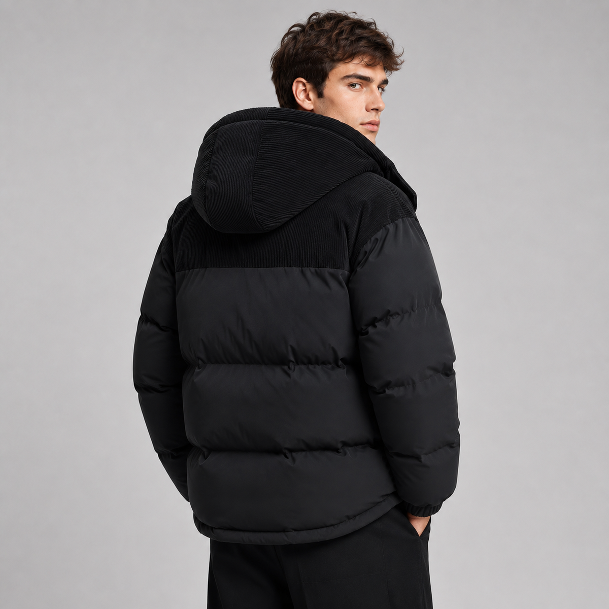Man wearing black padded hooded puffer jacket with ribbed texture on hood, shown from back view against gray background