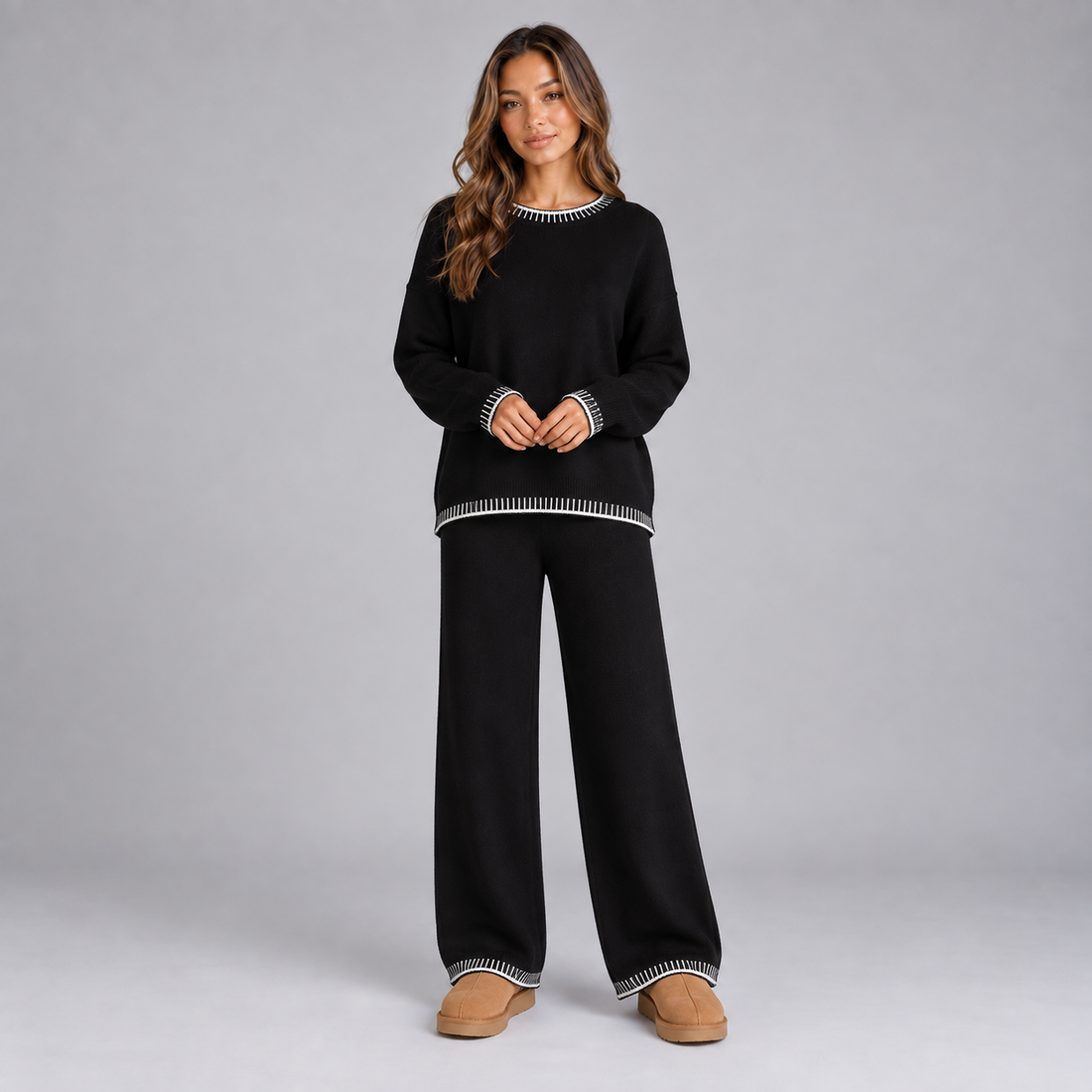 Woman wearing black knitted lounge set with white contrast trim on neckline, cuffs and hem, paired with tan slippers