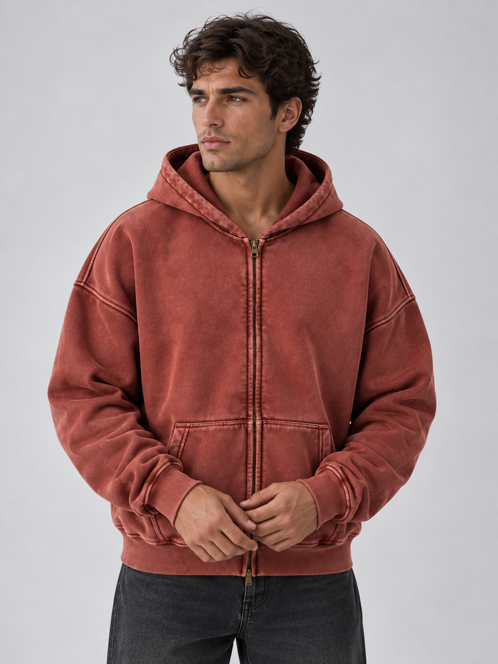 Man wearing rust red washed cotton full zip hooded jacket with ribbed cuffs and kangaroo pockets over dark jeans