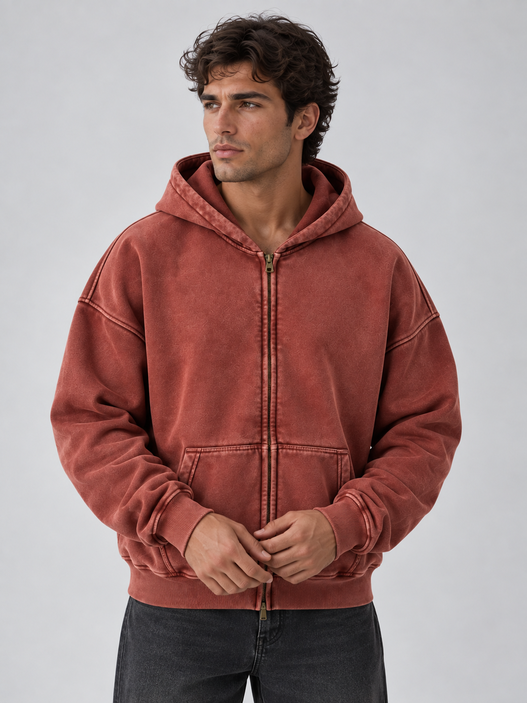 Man wearing rust red washed cotton full zip hooded jacket with ribbed cuffs and kangaroo pockets over dark jeans